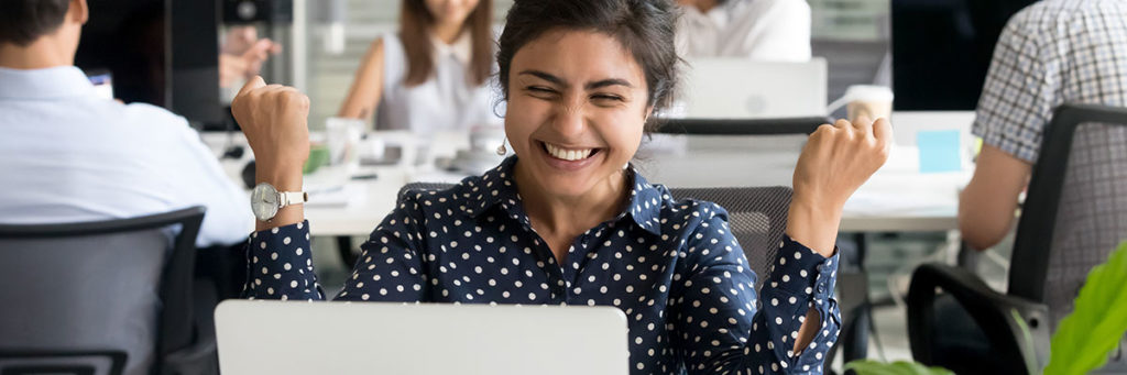 Student framför datorn som är glad efter att blivit antagen till traineeprogram