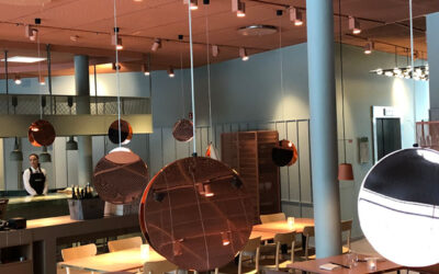 Modern restauranginteriör med kopparfärgade hängande lampor, öppet kök och personal i bakgrunden