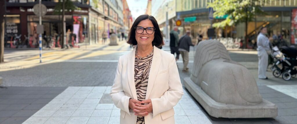 Kvinna i vit kavaj leende utomhus på Drottninggatan i Stockholm