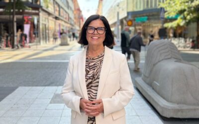 Kvinna i vit kavaj leende utomhus på Drottninggatan i Stockholm