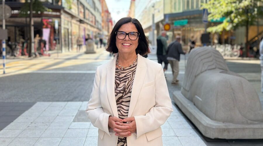 Kvinna i vit kavaj leende utomhus på Drottninggatan i Stockholm