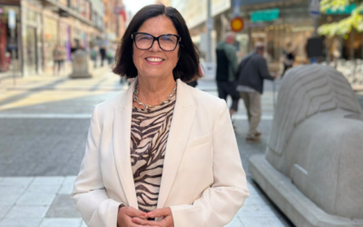 Leende kvinna i vit kavaj och zebramönstrad blus står utomhus på en gågata i centrala Stockholm.