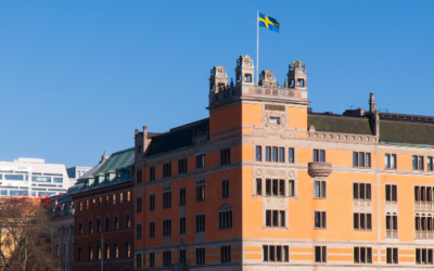 Historisk byggnad i orange fasad med svenska flaggan hissad på toppen mot klarblå himmel