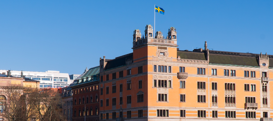 Historisk byggnad i orange fasad med svenska flaggan hissad på toppen mot klarblå himmel