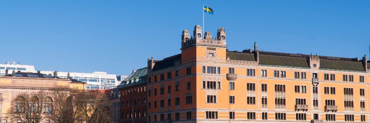 Historisk byggnad i orange fasad med svenska flaggan hissad på toppen mot klarblå himmel