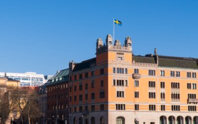 Historisk byggnad i orange fasad med svenska flaggan hissad på toppen mot klarblå himmel