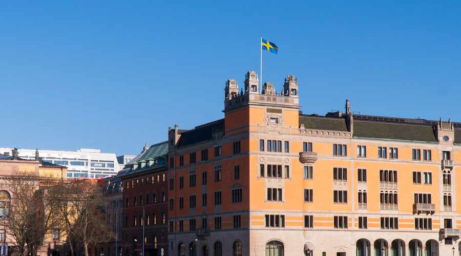 Historisk byggnad i orange fasad med svenska flaggan hissad på toppen mot klarblå himmel